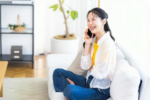 リビングでスマホで話す若い女性 スマホ,笑顔,電話の写真素材