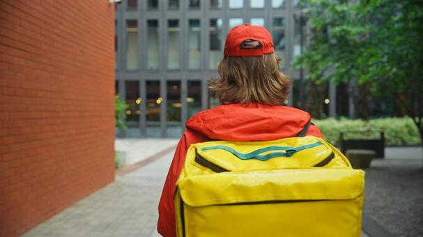 街なかにいる配達バッグを背負うフードデリバリーの男性の後ろ姿 配達,フードデリバリー,デリバリーの写真素材