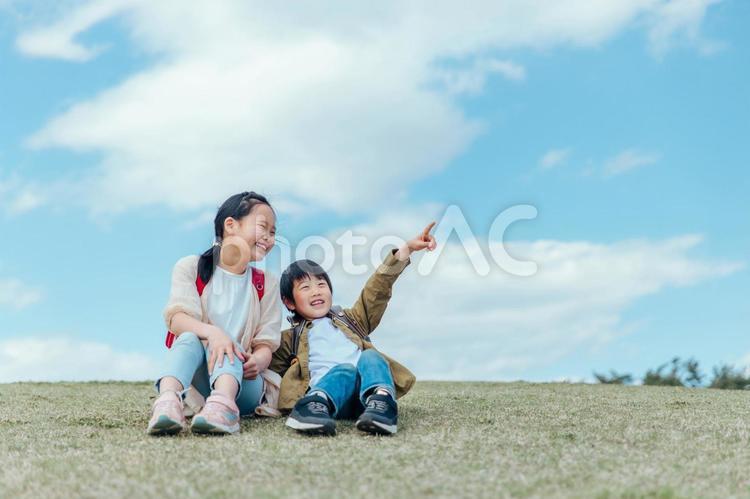 芝生に座る小学生（指差す） 小学生,子供,笑顔の写真素材
