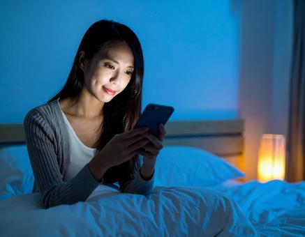 夜のベッドでスマホを見る女性の写真