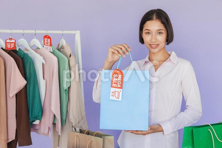 セールのタグの付いたハンガーに掛かった洋服と紙袋を見せる女性 セール,ショップ,女性の写真素材