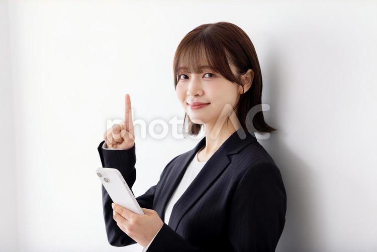 白壁に寄りかかりスマートフォンを使う女性 女性,ビジネスウーマン,スマートフォンの写真素材