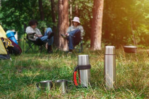 並ぶキャンプ道具と焚き火　日差し 水筒,マグカップ,鍋の写真素材