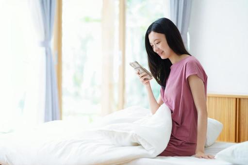 起床してスマホを見て微笑む女性 女性,スマートフォン,持つの写真素材