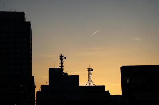 シルエットの街並みと飛行機雲のある夕空 シルエットの街並みと飛行機雲のある夕空の写真