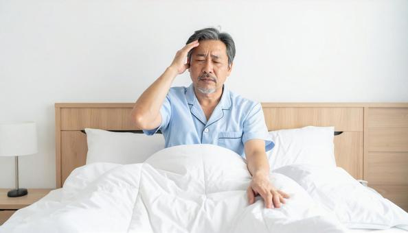 寝起きで座って頭を抱えるパジャマ姿の男性 寝起きで座って頭を抱えるパジャマ姿の男性の写真