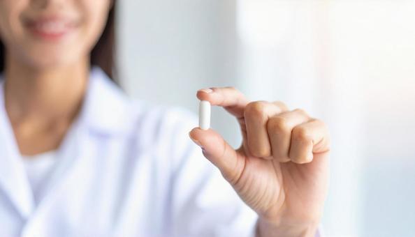 薬一錠を親指と人差し指で持つ女性 薬一錠を親指と人差し指で持つ女性の写真