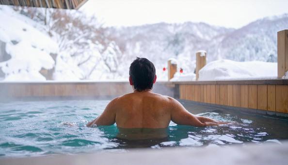 雪山の露天風呂に浸かる男性の後ろ姿 雪山の露天風呂に浸かる男性の後ろ姿の写真