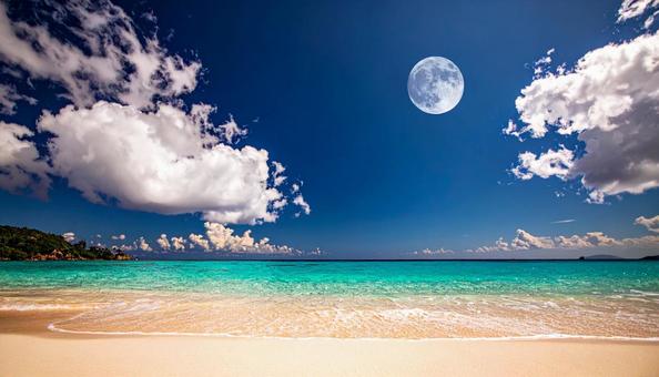 ビーチの青空に浮かぶ透けた白い月の写真