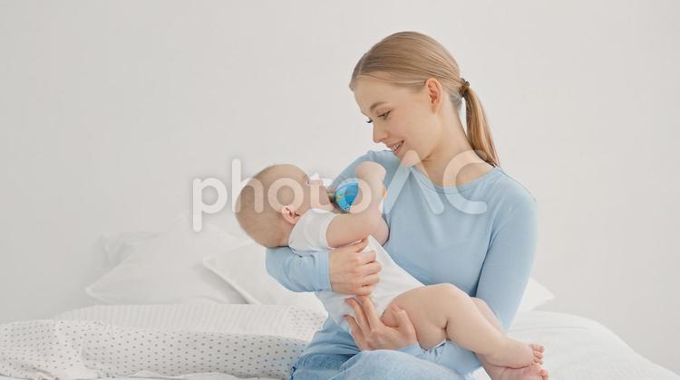 玩具を口に入れる赤ちゃんを抱っこしている女性 親子,抱っこ,見つめるの写真素材