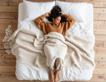 ブランケットをかけてベッドで眠る女性 ブランケットをかけてベッドで眠る女性の写真