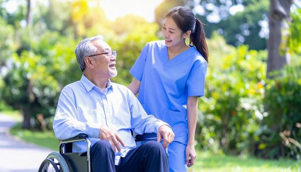 散歩する車椅子の高齢男性と女性介護士 散歩する車椅子の高齢男性と女性介護士の写真