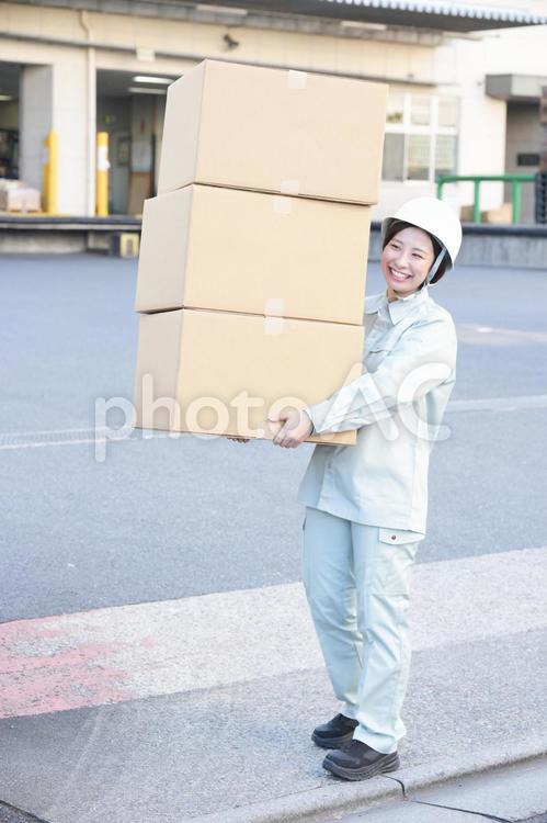 屋外でダンボール箱を重ねて運ぶ作業服の女性 女性,日本人,若者の写真素材