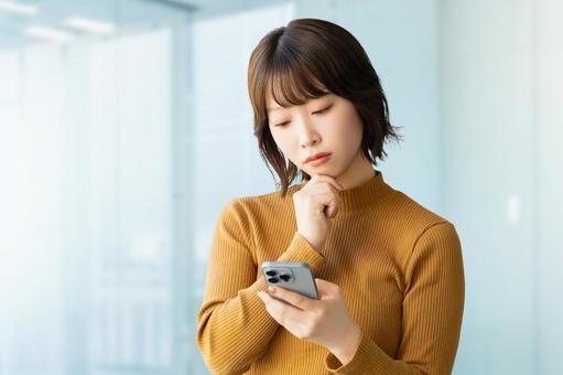 スマホを見て考える女性・ビジネスウーマン スマホを見て考える女性・ビジネスウーマンの写真