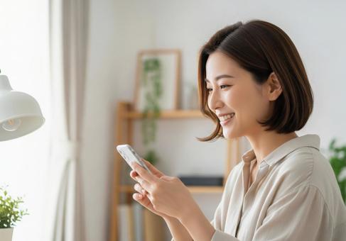 リビングで女性がスマホを見て微笑んでいる リビングで女性がスマホを見て微笑んでいるの写真