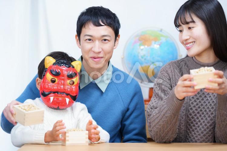 鬼の面をつけた男の子が男性の膝に座ってそれを見ている女性 家族,女性,男性の写真素材