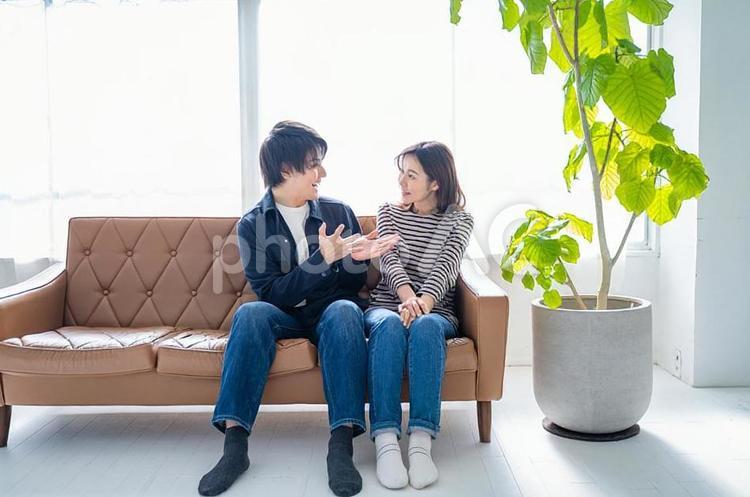 ソファに座り会話する夫婦-明るい観葉植物 夫婦,ソファ,リラックスの写真素材
