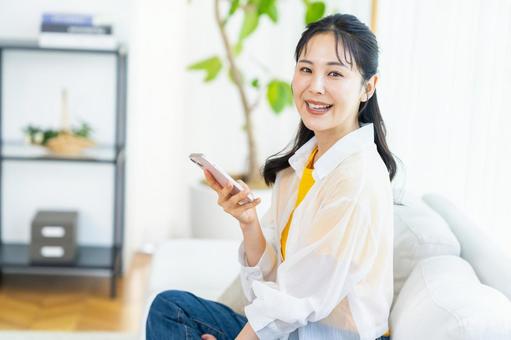 部屋でスマホを操作する女性 部屋でスマホを操作する女性 スマホ,笑顔,部屋の写真素材