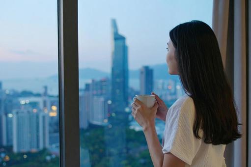 コーヒーを手に窓の外を眺める女性 コーヒーを手に窓の外を眺める女性の写真