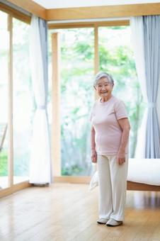 カメラ目線で立つベッド脇のおばあちゃん 女性,微笑む,笑顔の写真素材