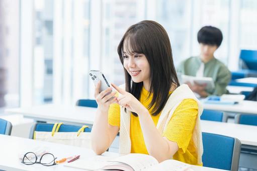 教室でスマホを見る女子大学生 スマホ,笑顔,大学生の写真素材