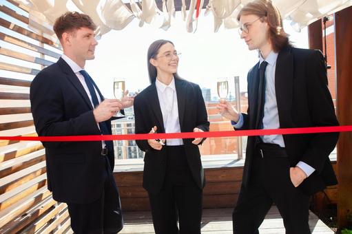 赤いテープの前で長髪の男性を見る2人 男女,テープカット,赤の写真素材