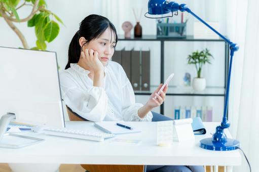 スマホを見ながら考えるビジネスウーマン スマホ,考える,悩むの写真素材