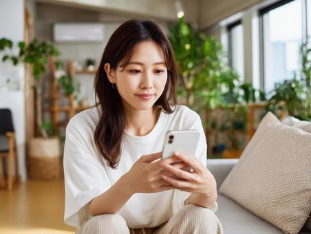 ソファーでスマートフォンを見つめる女性 ソファーでスマートフォンを見つめる女性の写真