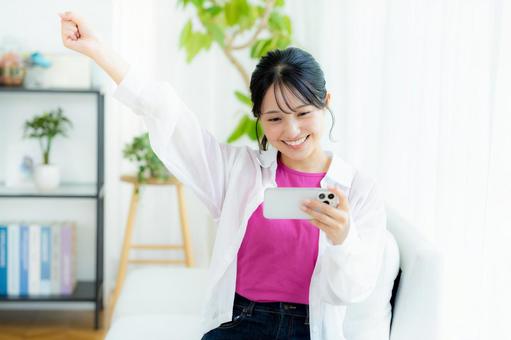 部屋でスマホを操作する若い女性 スマホ,笑顔,若い女性の写真素材