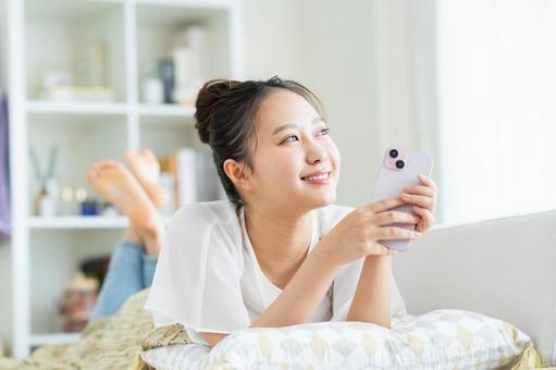 リビングでスマホを見る若い女性 リビングでスマホを見る若い女性 スマートフォン,笑顔,女性の写真素材
