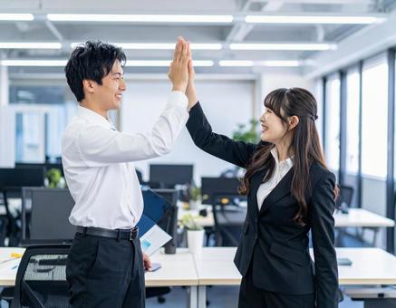 職場でハイタッチして喜ぶ男性と女性 職場でハイタッチして喜ぶ男性と女性の写真