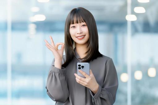 スマホを持ってOKポーズをする笑顔の女性 女性,ok,スマホの写真素材