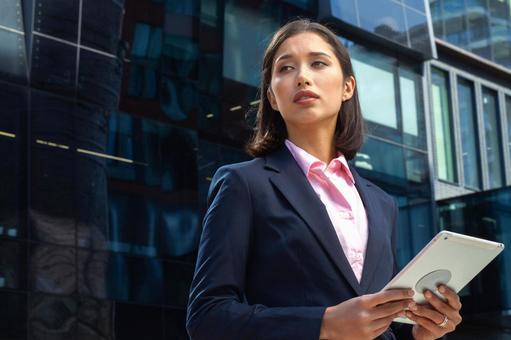 オフィスビルの外でタブレットを持って立つスーツのアジア人ビジネスウーマン ビジネスウーマン,ビジネス,女性の写真素材