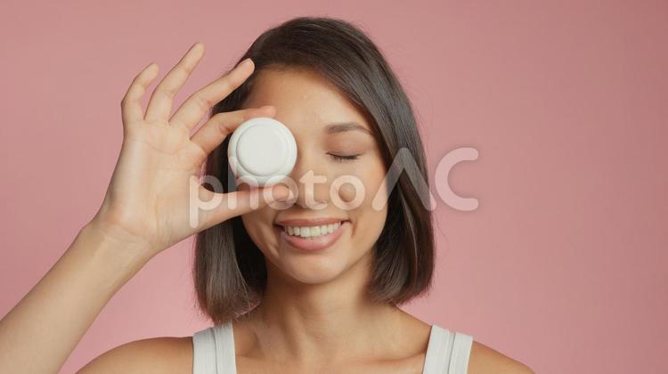 クリームの容器を目に当てている笑顔の女性 女性,外国人,アジア人の写真素材