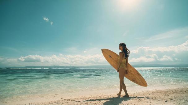 海辺の砂浜でサーフボードを抱え歩く女性 海辺の砂浜でサーフボードを抱え歩く女性の写真
