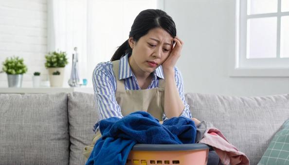 洗濯物をたたみ家事にストレスを抱える女性 洗濯物をたたみ家事にストレスを抱える女性の写真