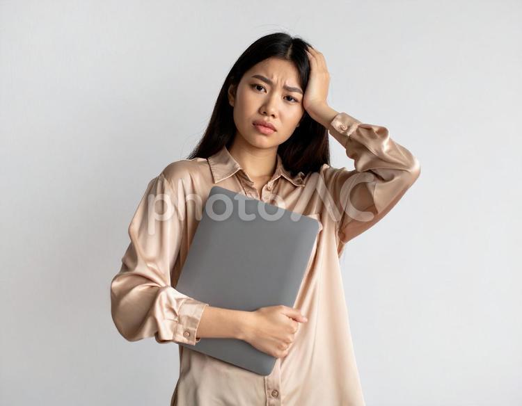 ノートパソコンを抱えて困った表情の女性 ストレス,困惑,困ったの写真素材