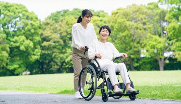 車椅子を押す日本人の女性ヘルパーと高齢者 車椅子を押す日本人の女性ヘルパーと高齢者の写真