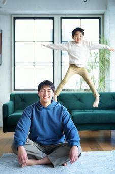 カメラ目線でソファーでジャンプする男の子と座っている男性 カメラ目線でソファーでジャンプする男の子と座っている男性の写真