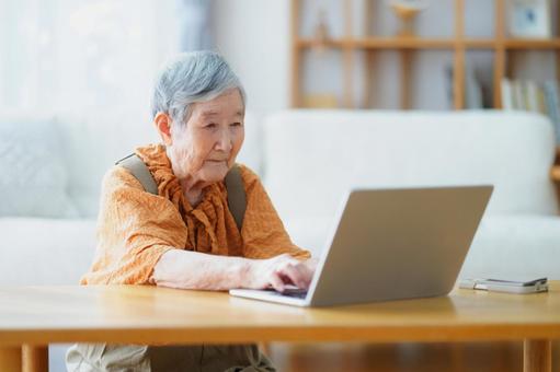 リビングでパソコン作業をする高齢女性 女性,ノートパソコン,座るの写真素材