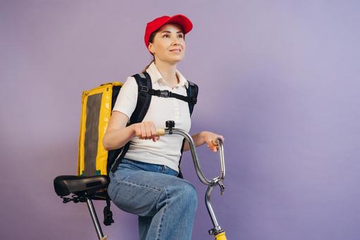 自転車に乗るフードデリバリーの女性（紫背景） 配達,フードデリバリー,デリバリーの写真素材