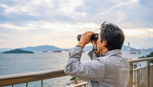 双眼鏡で海の先を見ている日本人男性 双眼鏡で海の先を見ている日本人男性の写真