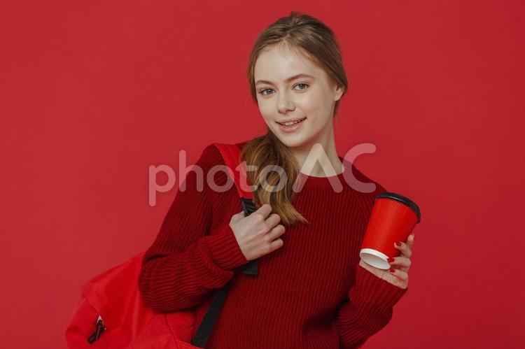 コーヒーとリュックを持った女性（上半身） 女性,赤,金髪の写真素材