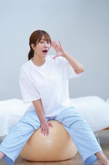 バランスボールに座りカメラ目線で呼ぶ女性 女性,呼ぶ,叫ぶの写真素材