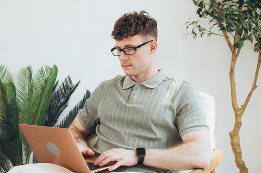 椅子に座って膝の上でノートパソコンを使うポロシャツの男性 男性,外国人,欧米人の写真素材