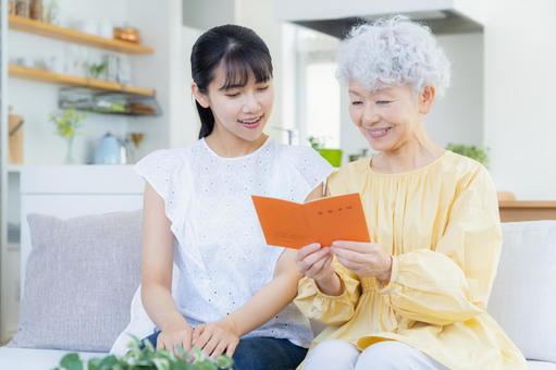 リビングで年金手帳を見る孫と祖母 リビングで年金手帳を見る孫と祖母 家族,シニア,女性の写真素材