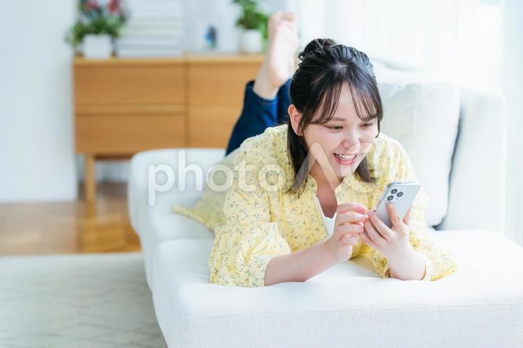 部屋でスマホを操作する若い女性 スマホ,若い女性,笑顔の写真素材