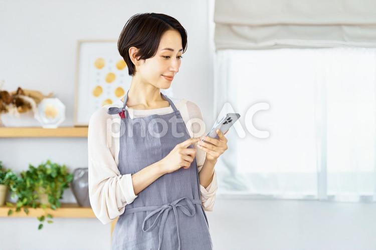 スマートフォンを見る主婦　リビング スマホ,主婦,エプロンの写真素材