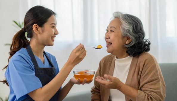 ゼリーをシニア女性に食べさせる介護士 ゼリーをシニア女性に食べさせる介護士の写真