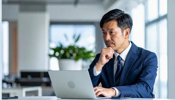 パソコンの前で悩む男性ビジネスマンの写真